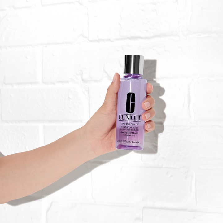 Clinique Take the Day Off Makeup Remover 125 ml effektiv makeupfjerner i lilla flaske holdt mod en hvid væg