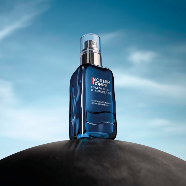 Biotherm Homme Force Supreme Blue Serum 60 ml opstrammende ansigtsserum i blå glasflaske på en sten mod en klar himmel