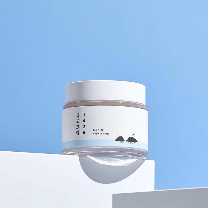 Round Lab 1025 Dokdo Cream 80 ml fugtgivende ansigtscreme i hvid krukke med ø-illustration på blå baggrund.