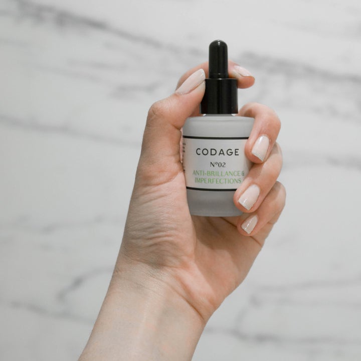 Codage Paris The Serum N°02 30 ml matterende ansigtsserum holdt i en hånd mod marmorbaggrund.