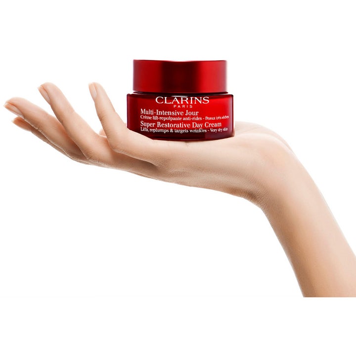 Clarins Super Restorative Day Cream 50 ml fugtgivende ansigtscreme i rød glaskrukke holdt i en hånd.