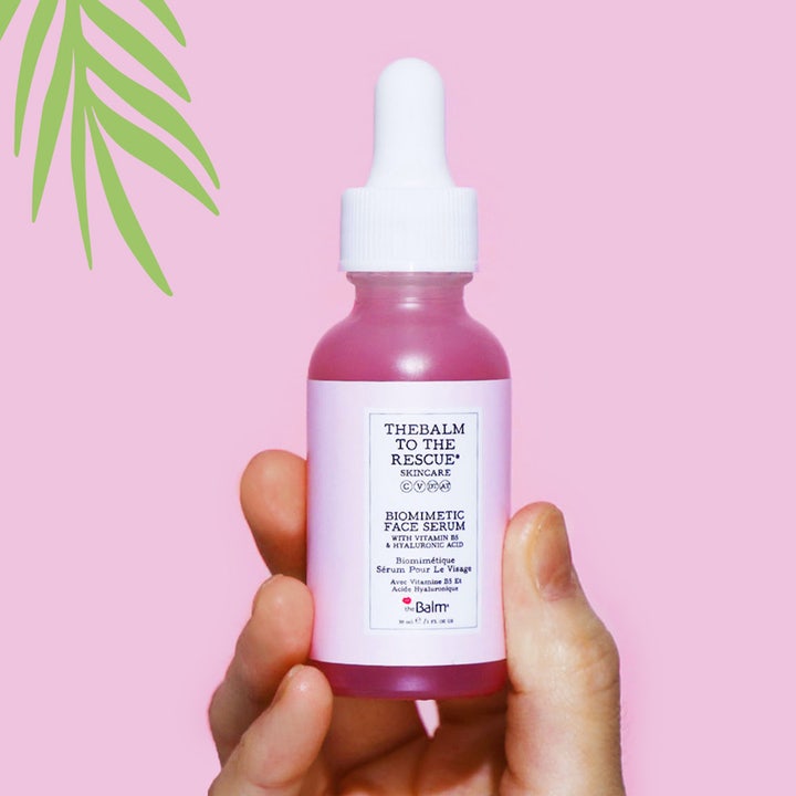 the Balm theBalm to the Rescue Biomimetic Face Serum 30 ml fugtgivende serum i lyserød glasflaske holdt i en hånd