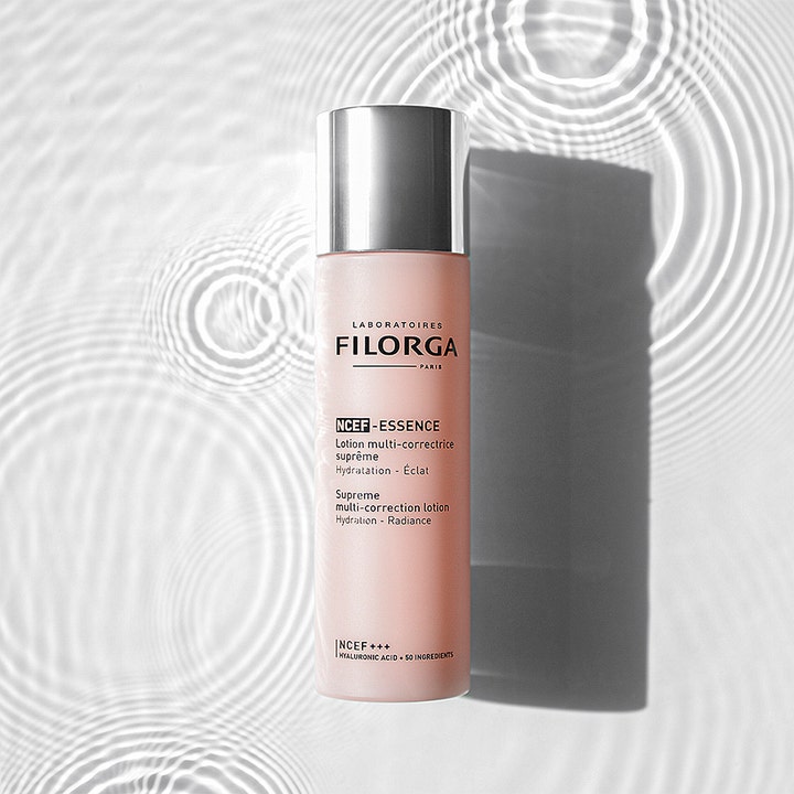 Filorga NCEF-Essence 150 ml fugtgivende essence giver glød i frostet lyserød flaske med sølvlåg på vandoverflade.