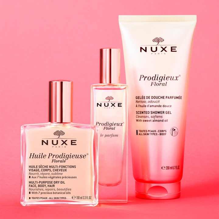 Nuxe Huile Prodigieuse Floral 100 ml fugtgivende kropsolie vist med showergel og parfume på pink baggrund.