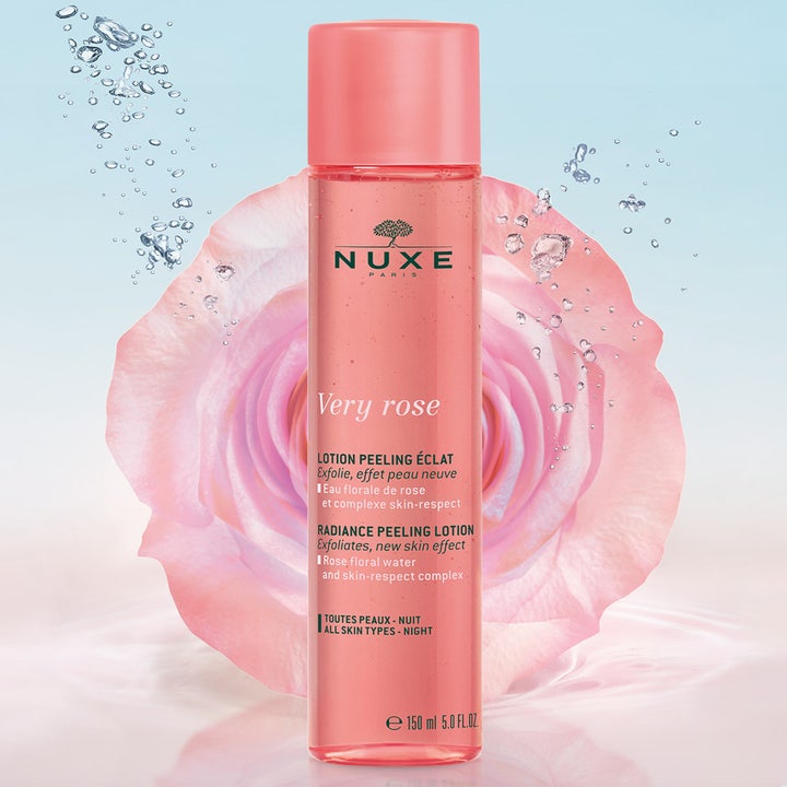 Nuxe Very Rose Peeling Lotion 150 ml eksfolierende peeling i pink flaske foran en stor lyserød rose