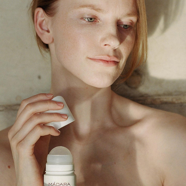 MÁDARA Herbal Deodorant 50 ml giver naturlig friskhed i en hvid roll-on holdt af en kvinde.