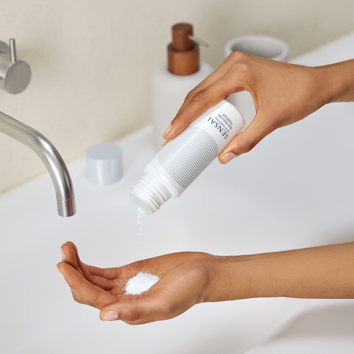 Sensai Silky Purifying Silk Peeling Powder 40 g eksfolierende ansigtsskrub der hældes fra hvid flaske i hånden