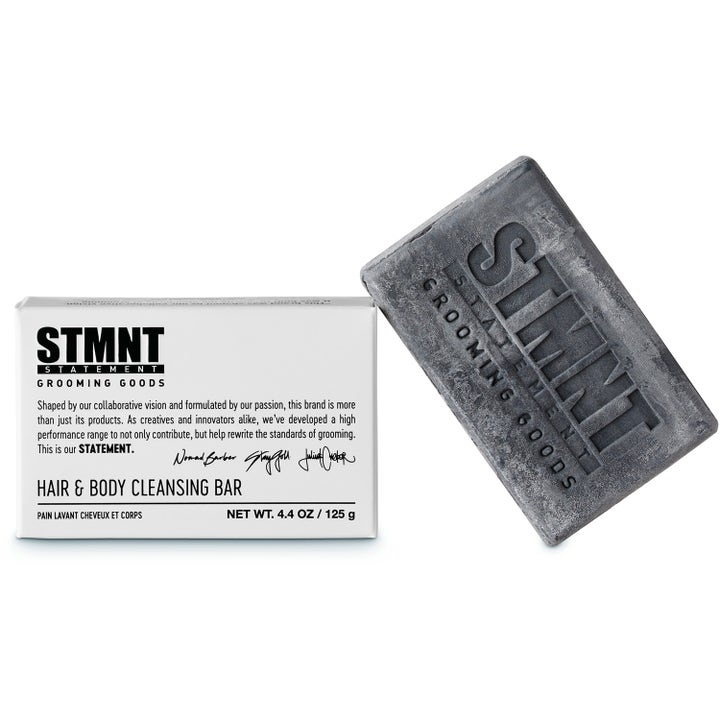 STMNT Grooming Goods Hair & Body Soapbar 125 g rensende fast sæbe vist som en mørkegrå bar ved siden af sin hvide æske.