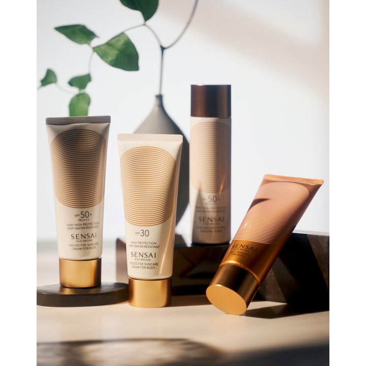 Sensai Silky Bronze Self Tanning For Body 150 ml selvbruner i bronzefarvet tube i et lyst miljø med grønne blade.