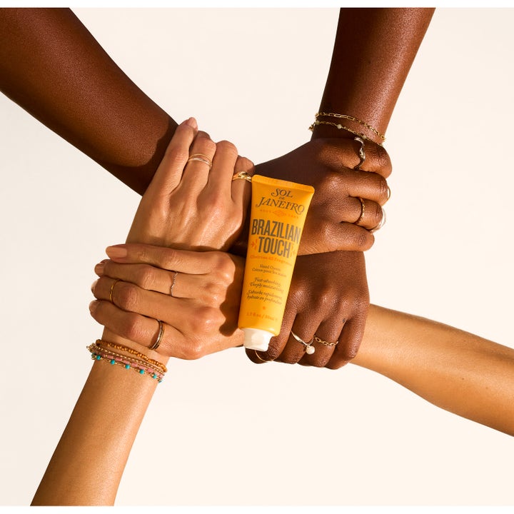 Sol de Janeiro Brazilian Touch Hand Cream 50 ml fugtgivende håndcreme i gul tube holdt af hænder med forskellige hudtoner