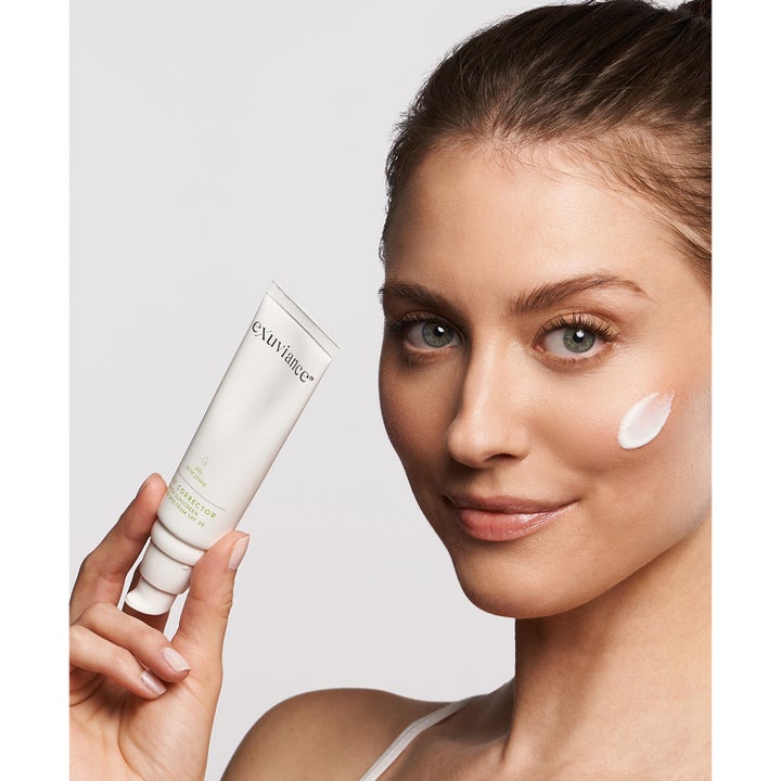 Exuviance Daily Corrector SPF35 40 g solcreme på hvid tube holdt af kvinde med creme på kinden