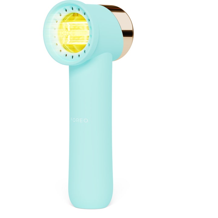 Foreo hudplejeenhed til fornyende lysbehandling i mintblå med guld detalje og et klart gult LED-lys.