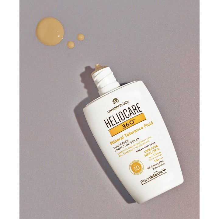 Heliocare Mineral Tolerance Fluid SPF 50 50 ml beskyttende solcreme i hvid flaske med beige teksturdråber på grå flade