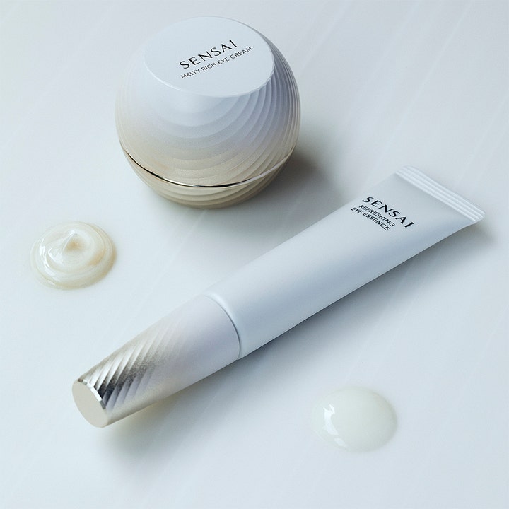 Sensai Total Eye Treatment 35 ml øjencreme og essence med rillet hvid krukke og tube samt teksturprøver.