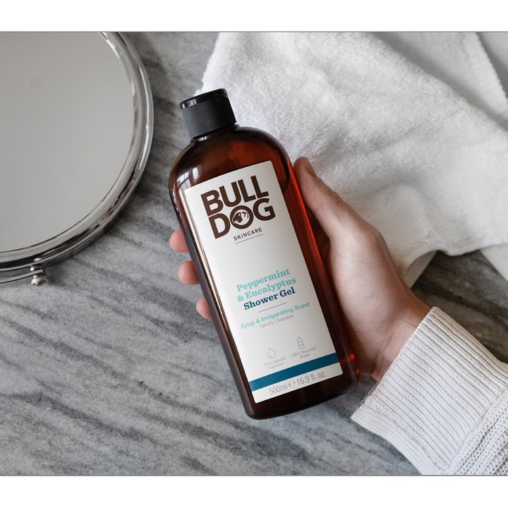 Bulldog Peppermint & Eucalyptus Shower Gel 500 ml opfriskende kropsvask i brun flaske holdt ved et spejl og hvidt håndklæde.