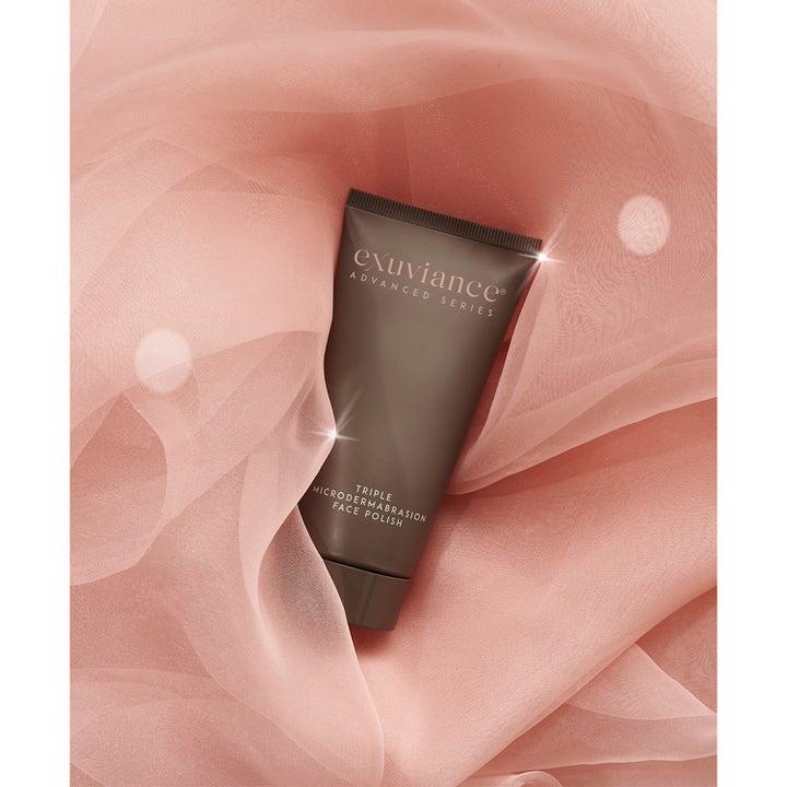 Exuviance Triple Microdermabrasion Face Polish 75 g eksfolierende peeling i brun tube på elegant lyserødt stof.