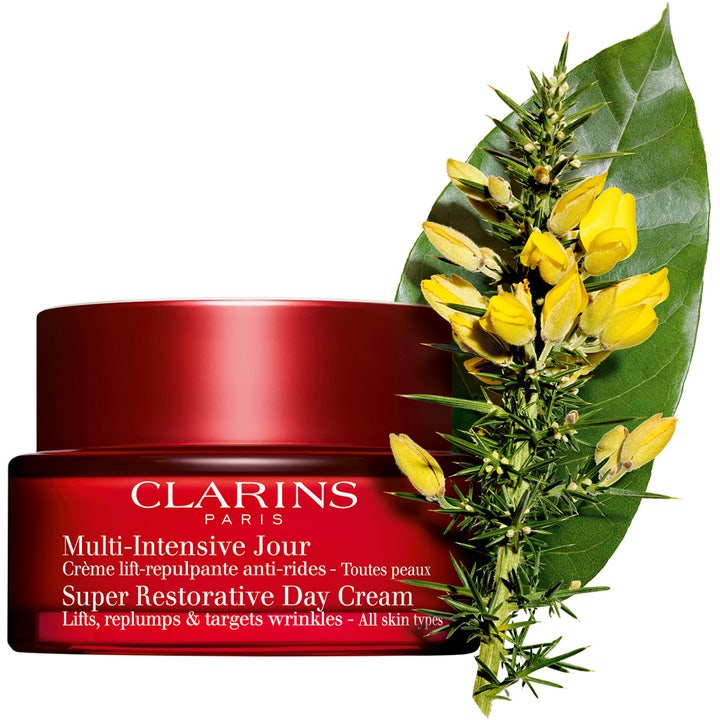 Clarins Super Restorative Day Cream 50 ml i rød krukke ved siden af en grøn gren med små gule blomster.