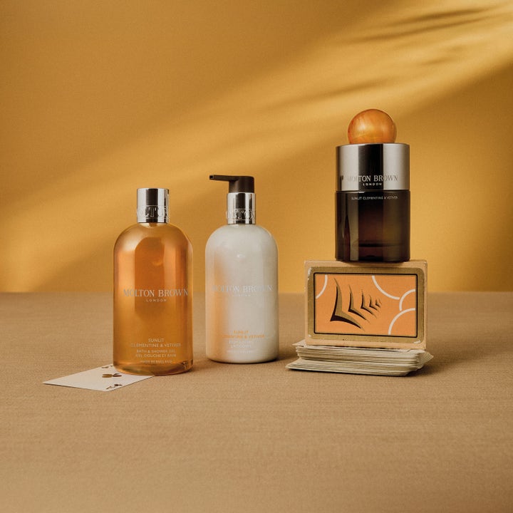 Molton Brown Sunlit Clementine & Vetiver 300 ml fugtgivende bodylotion i hvid pumpeflaske i et varmt, gyldent miljø