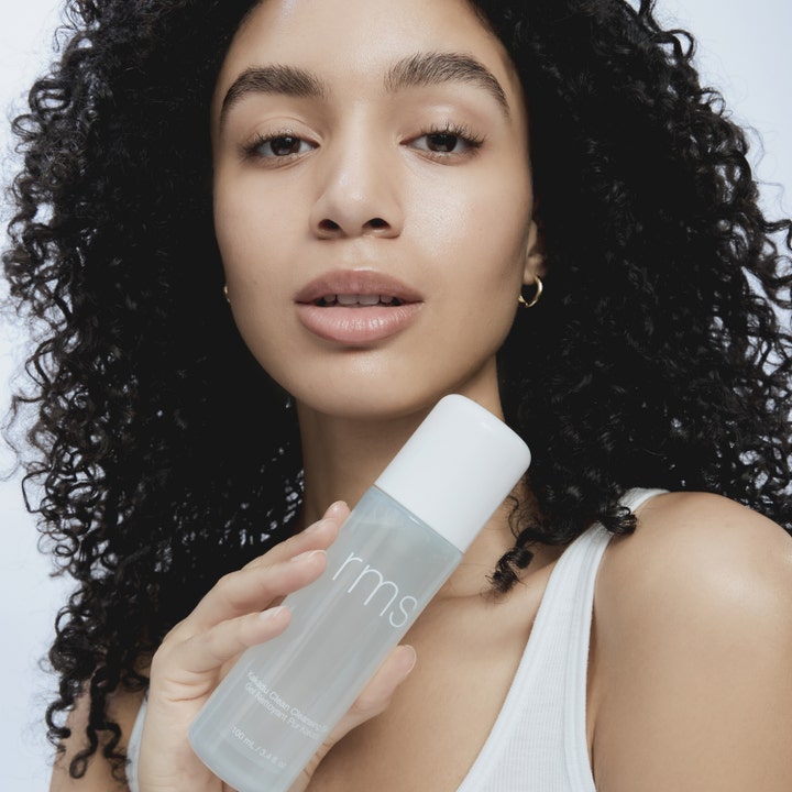 RMS Beauty Kakadu Clean Cleansing Gel 100 ml opfriskende ansigtsrens i frostet flaske holdt af kvinde med krøller