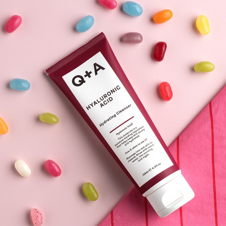 Q+A Hyaluronic Acid Gel Cleanser 125 ml fugtgivende ansigtsrens i bordeaux tube med farverige gelébønner på lyserød bund
