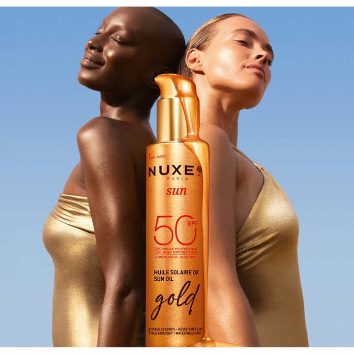 Nuxe Sun Tanning Oil Gold 150 ml solcreme med SPF 50 giver glød vist i guldflaske med to kvinder i guld badetøj.