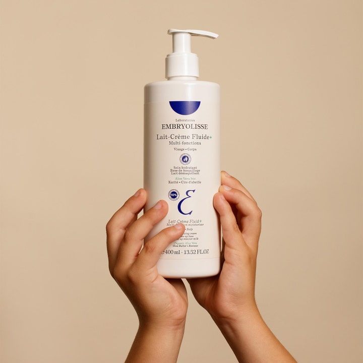Embryolisse Lait-Crème Fluid+ 400 ml fugtgivende ansigtscreme og kropspleje i hvid pumpeflaske holdt af to hænder