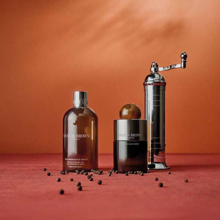 Molton Brown Re-Charge Black Pepper Body Wash 300 ml og parfume ved siden af en sølvfarvet peberkværn.