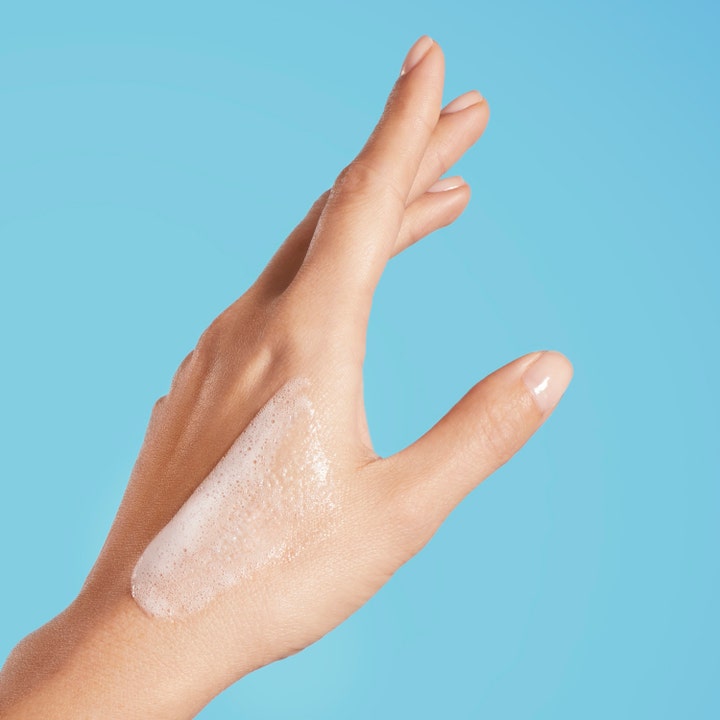 Biotherm Oil Therapy Baume Corps 200 ml fugtgivende badegel med hvidt skum på en hånd mod en blå baggrund