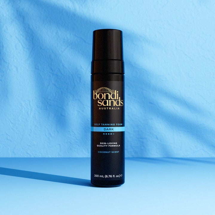 Bondi Sands Self Tanning Foam Dark 200 ml selvbruner i sort flaske skaber en dyb glød mod lyseblå baggrund.