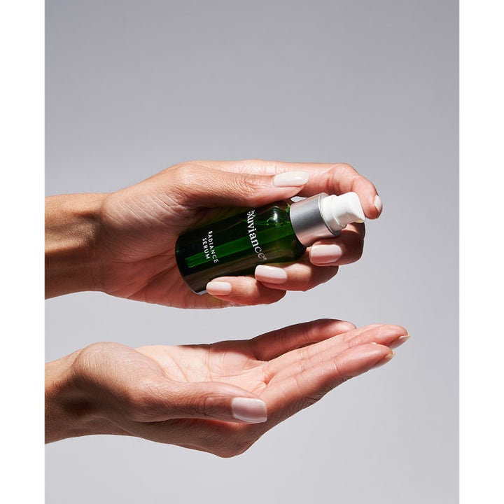 Exuviance Radiance Serum 30 ml giver glød i en grøn glasflaske med sølvpumpe holdt i hænderne