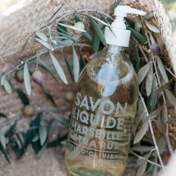 Compagnie de Provence Liquid Marseille Soap Olive Wood 495 ml håndsæbe i klar glasflaske med olivengrene i en kurv