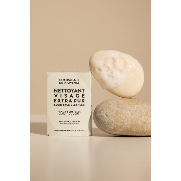 Compagnie de Provence Solid Face Cleanser 85 g beroligende ansigtsrens i æske ved siden af sten med cremet hvidt skum