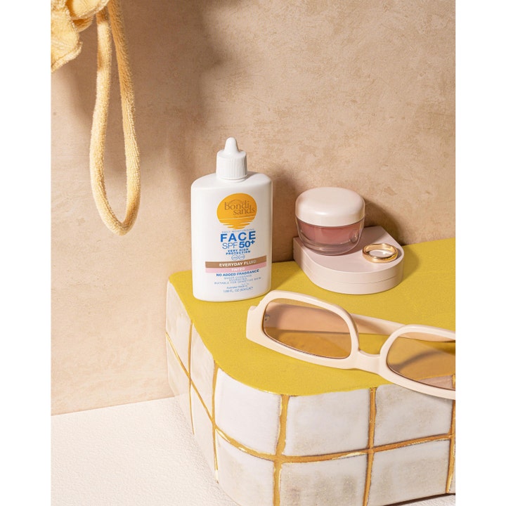 Bondi Sands SPF50+ Everyday Tinted Face Fluid 50 ml solcreme til ansigtet i hvid flaske ved siden af beige solbriller