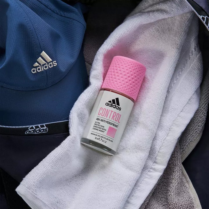 Adidas Control 48H Anti-Perspirant 50 ml roll-on i glasflaske med lyserødt låg på et hvidt håndklæde og blå kasket