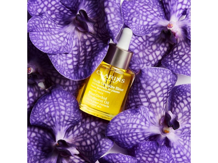 Clarins Blue Orchid Face Treatment Oil 30 ml fugtgivende ansigtsolie i glasflaske omgivet af lilla orkidéer