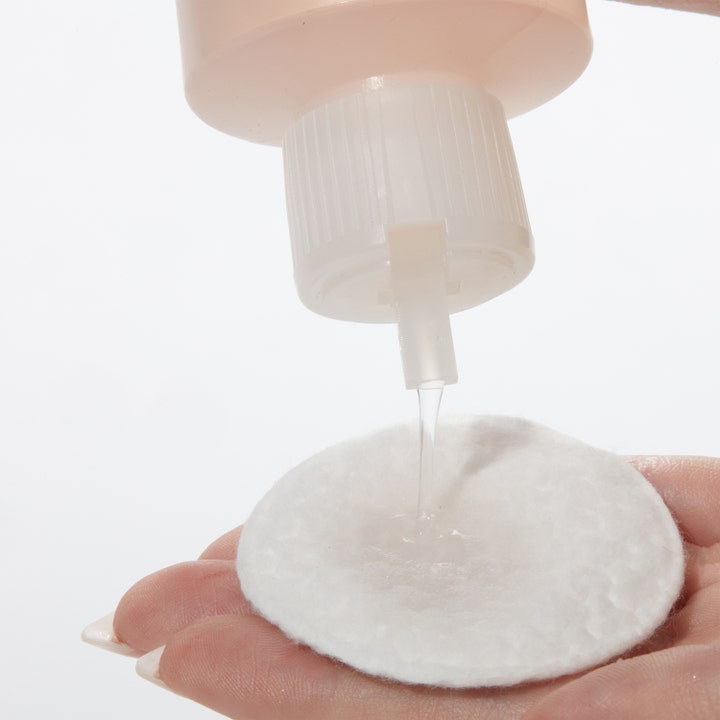 Mario Badescu Witch Hazel & Rosewater Toner 236 ml ansigtsvatten hældes fra flasken på en hvid vatrondel i hånden.