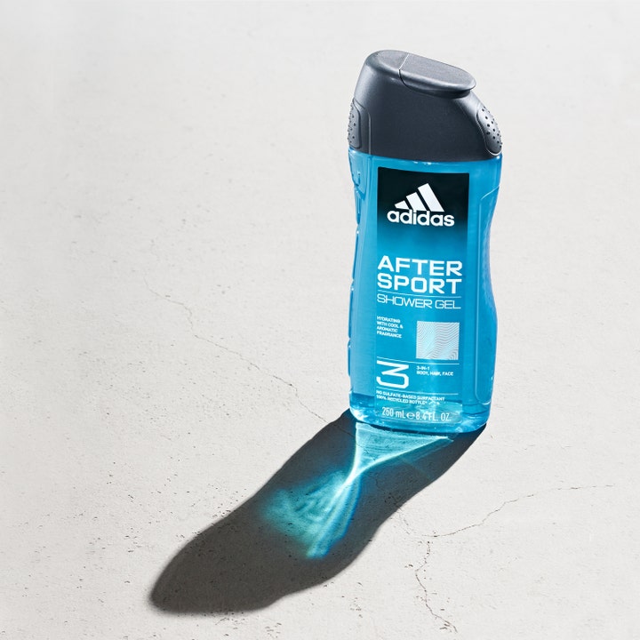 Adidas After Sport 250 ml 3-i-1 shower gel giver friskhed i en blå gennemsigtig flaske med mørkt låg på grå flade.