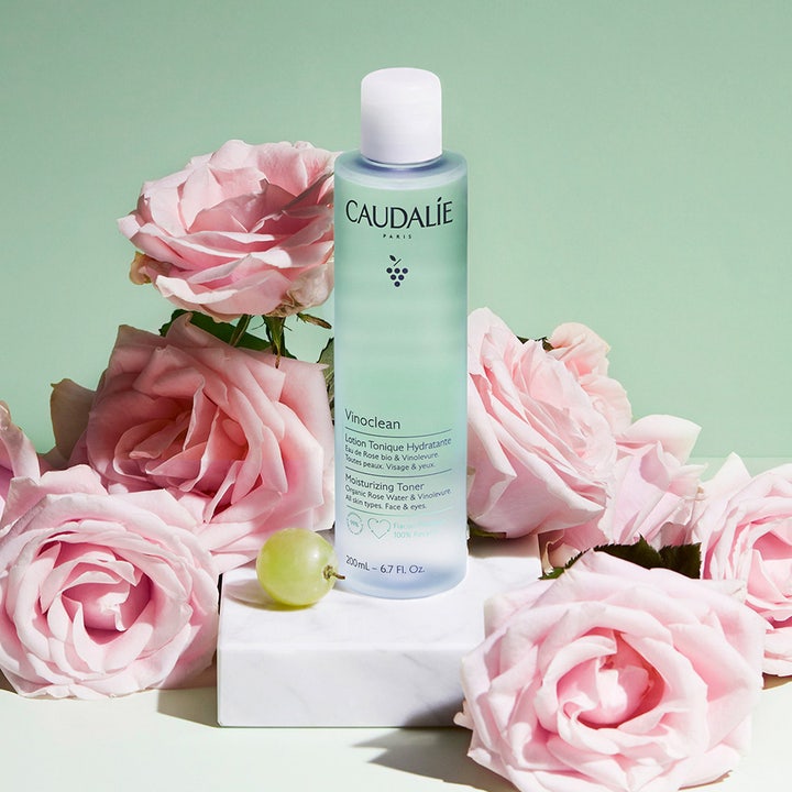 Caudalie Vinoclean Moisturizing Toner 200 ml i lyseblå flaske omgivet af lyserøde roser og en vindrue.