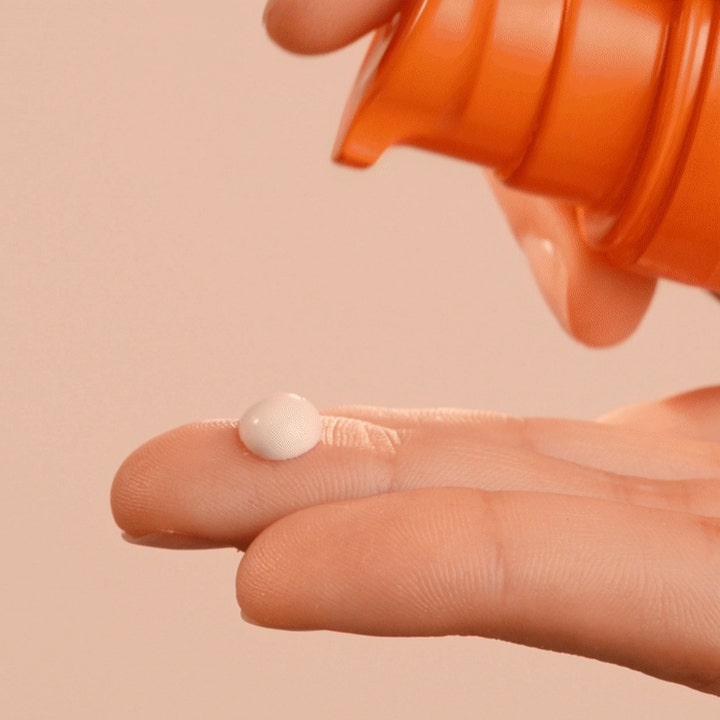 Lancaster Sun Care Face Fluid Cream 30 ml solcreme til ansigtet med hvid creme på en finger fra orange pumpe