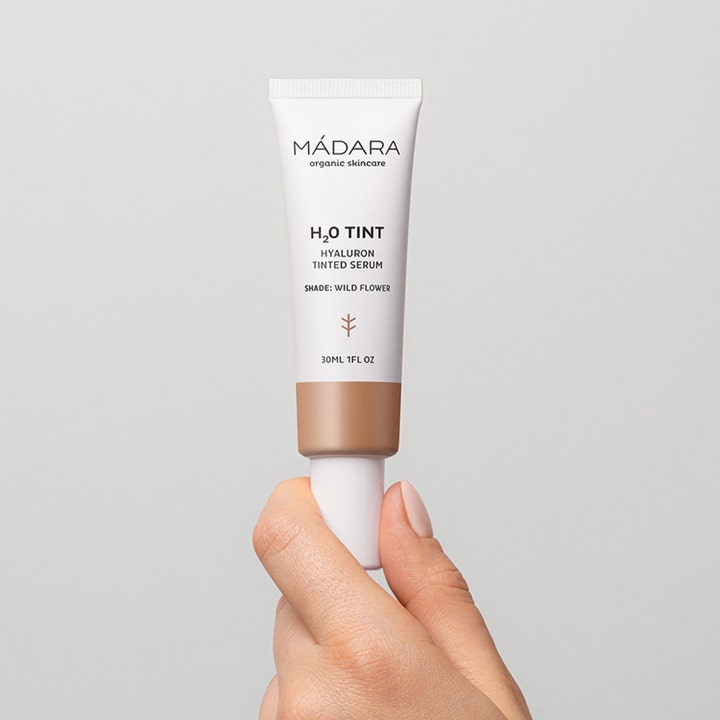 MÁDARA H2O Tint Hyaluron Tinted Serum 30 ml fugtgivende serum i hvid tube holdt af en hånd.