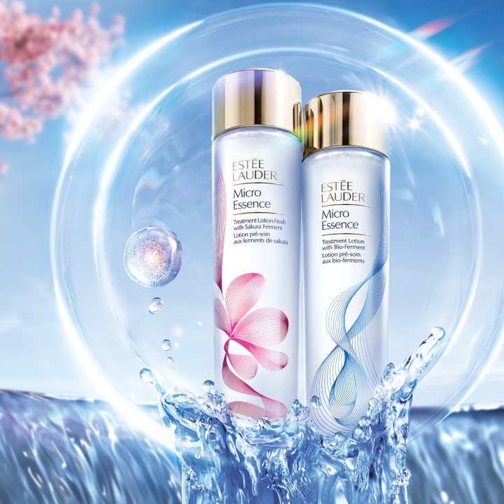 Estée Lauder Micro Essence 200 ml fugtgivende essence i flasker med guldhætter omgivet af vandstænk og en lysende boble.