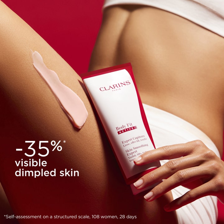 Clarins Body Fit Active 200 ml opstrammende bodylotion mod appelsinhud med lyserød creme på et lår ved siden af tuben