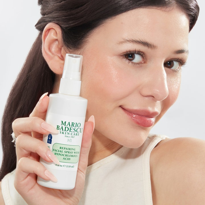 Mario Badescu Repairing Facial Spray 118 ml ansigtsmist holdt af en person med glødende hud