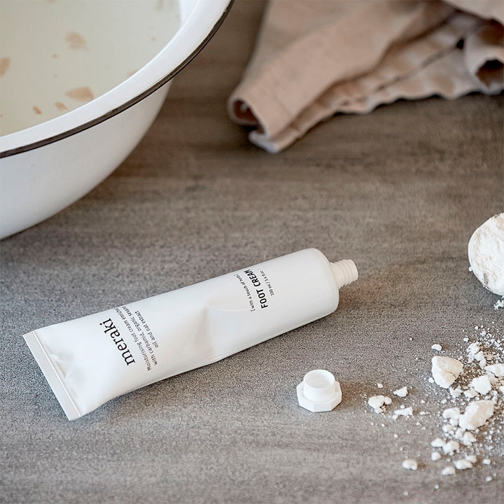 Meraki Foot Cream 100 ml plejende fodcreme i hvid tube med urter ved siden af et afslappende fodbad