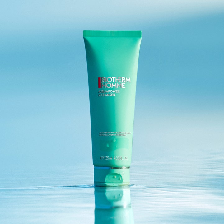 Biotherm Homme Aquapower Cleanser 125 ml opfriskende ansigtsvask i grøn tube på en spejlende blå overflade