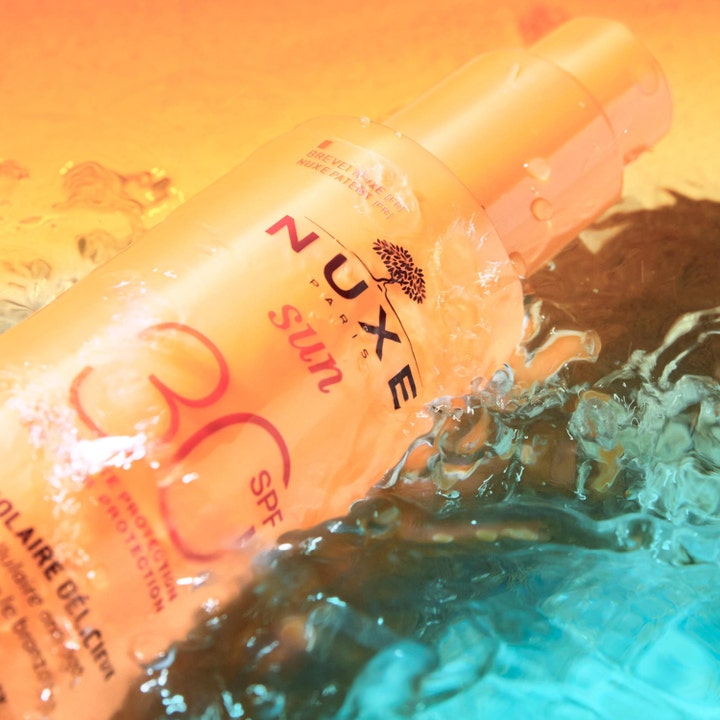 Nuxe Sun Spray SPF30 184 g solcreme til ansigtet i orange flaske der beskytter huden i sprøjtende blåt vand.