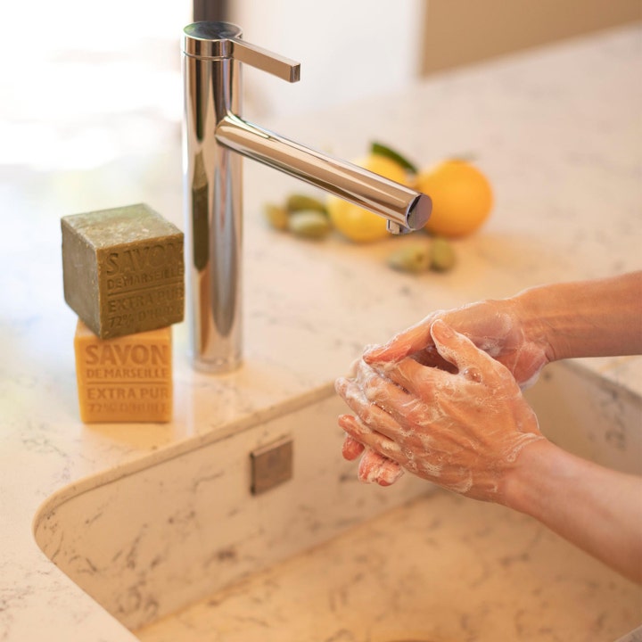Compagnie de Provence Cube Of Marseille Soap Olive 400 g marseille sæbe viser hænder der vaskes med skum ved en vask.