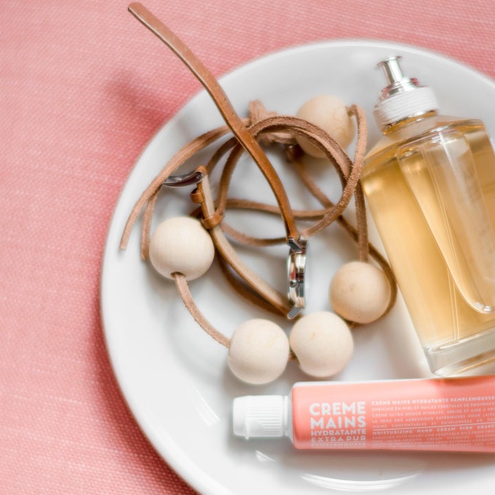 Compagnie de Provence Pink Grapefruit 30 ml fugtgivende håndcreme i tube med ur og parfume på en hvid tallerken.