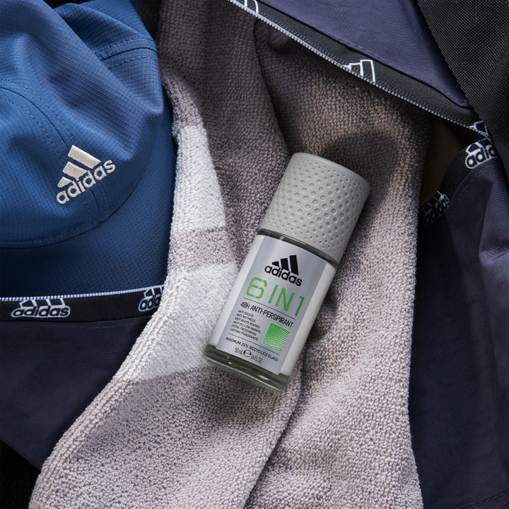 Adidas Cool & Dry 6 In 1 Roll-on Deodorant 50 ml antiperspirant ligger på et gråt håndklæde ved siden af en blå kasket.