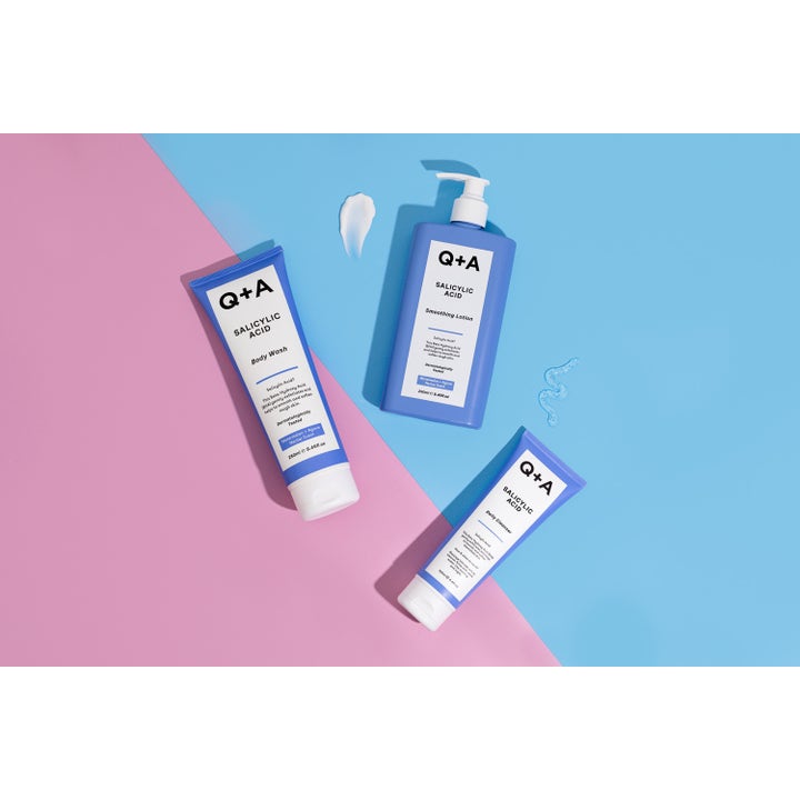 Q+A Salicylic Acid Body Wash 250 ml eksfolierende kropsvask i blå tube vist med hudplejeserie på lyserød og blå baggrund